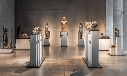 Ausstellungsraum im Staatlichen Museum Ägyptischer Kunst in München mit Skulpturen und Büsten aus Stein. Zentral steht eine monumentale Statue eines Pharaos, flankiert von weiteren Figuren in symmetrischer Anordnung unter dezentem Licht.